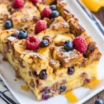 Golden brown French toast casserole topped with powdered sugar and fresh berries, served in a white baking dish.