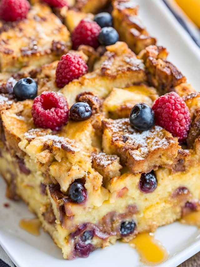 Golden brown French toast casserole topped with powdered sugar and fresh berries, served in a white baking dish.