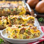 Close-up view of a golden-brown sausage and egg breakfast casserole, topped with melted cheese and garnished with fresh herbs, served in a baking dish.